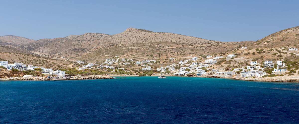 A coastal village with white buildings nestled against a backdrop of mountains.