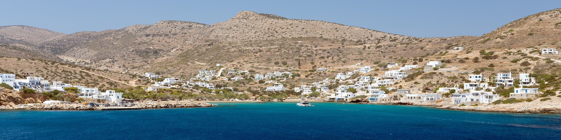 A coastal village with white buildings nestled against a backdrop of mountains.