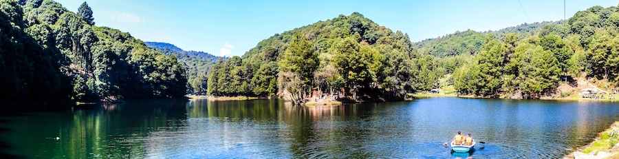 panoramic of lake with boat in the water, green forest around and blue sky in dam of the llano, villa del carbon state of mexico