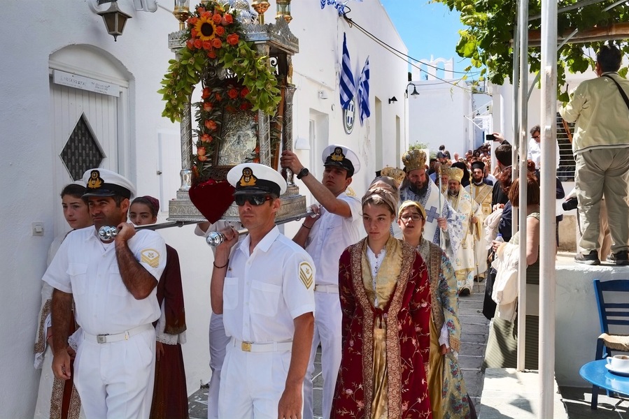 Apollonia Απολλωνία, Sifnos. The biggest festival of all is that of the patron saint of the island, Panagia Chrysopigi, celebrated on Ascension Day, attended by many people from all over the island and beyond. In the afternoon of the day before, the miracle icon of Zoodochou Pigis (the Life-Giving Spring) is ‘transported’ from the home of the ‘panigiras’ and the festival procession, with the clergy and the faithful, follows the path to the Holy Church of Agios Georgios in Kamares where the liturgy is held. Then the clergy, with the ‘panigiras’ carrying the icon, board the ferry that each year on this day adds the sacred rock of Chrysopigi to its route from Piraeus. The ship does not carry the believers because disembarkation is potentially dangerous. The crowd of believers, local people and visitors, take the road to Chrissopigi where the arrival of the icon is greeted with great enthusiasm, and the celebrations are honoured by music of the Coast Guard band.