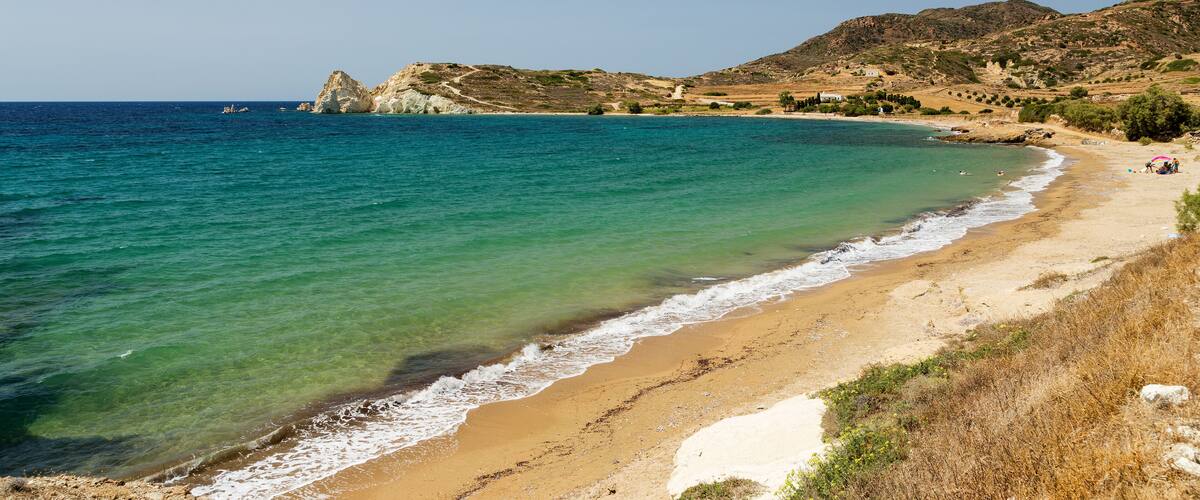 A coastal landscape with clear turquoise waters, a sandy beach, and rocky hills in the background.