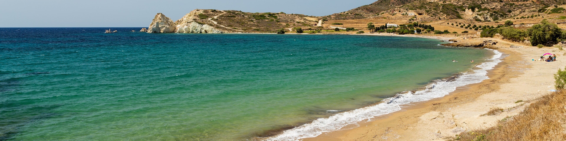 A coastal landscape with clear turquoise waters, a sandy beach, and rocky hills in the background.