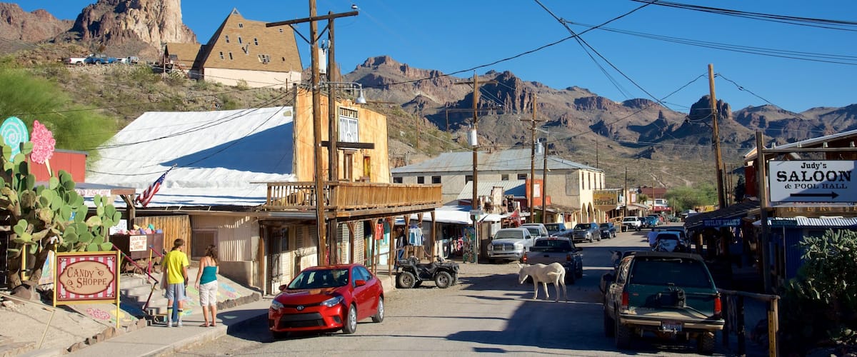 A small town street with a red car, a horse, and a mountain in the background.