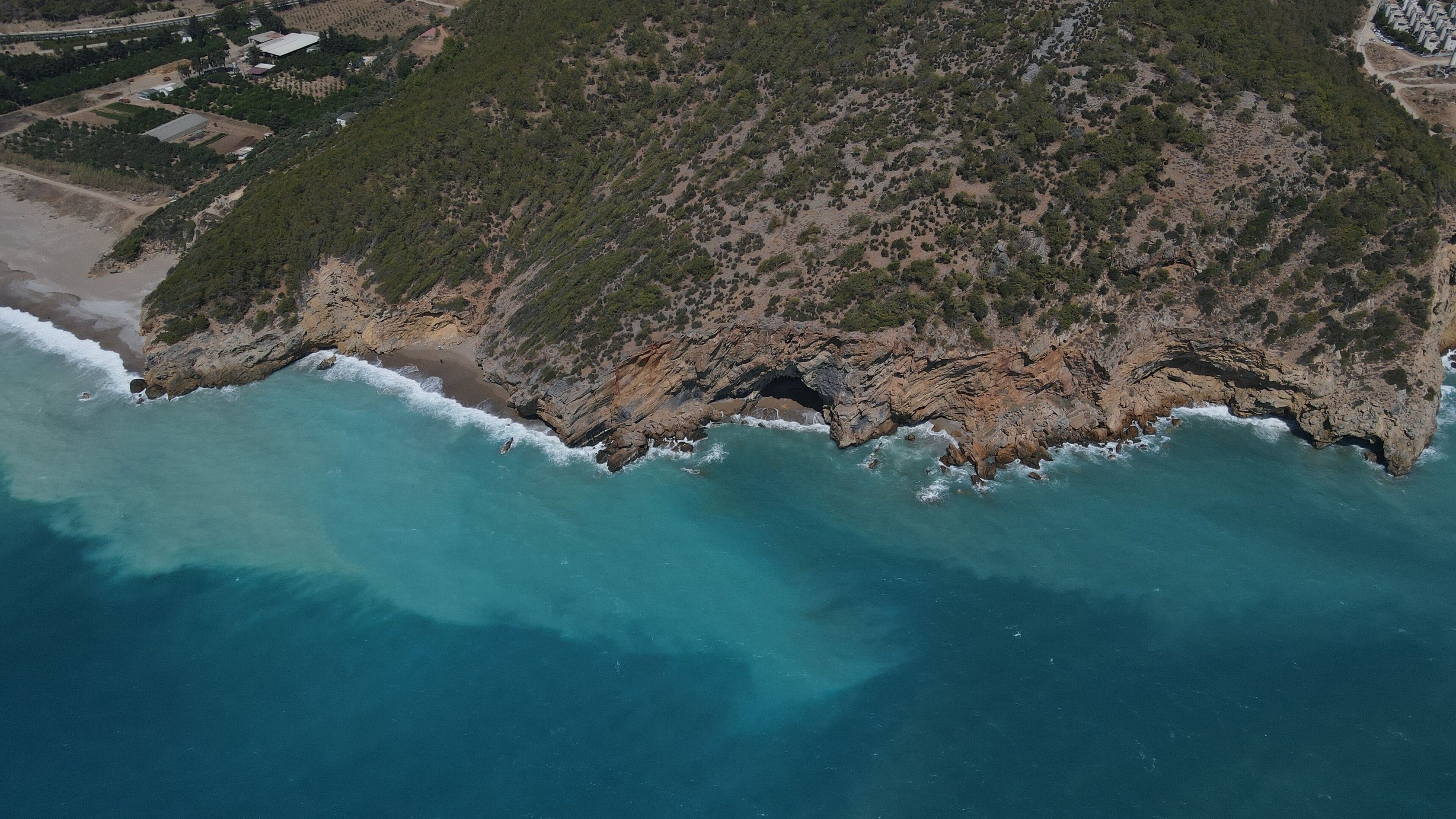 A coastal landscape with a rocky shoreline, clear turquoise waters, and a dense forested area.