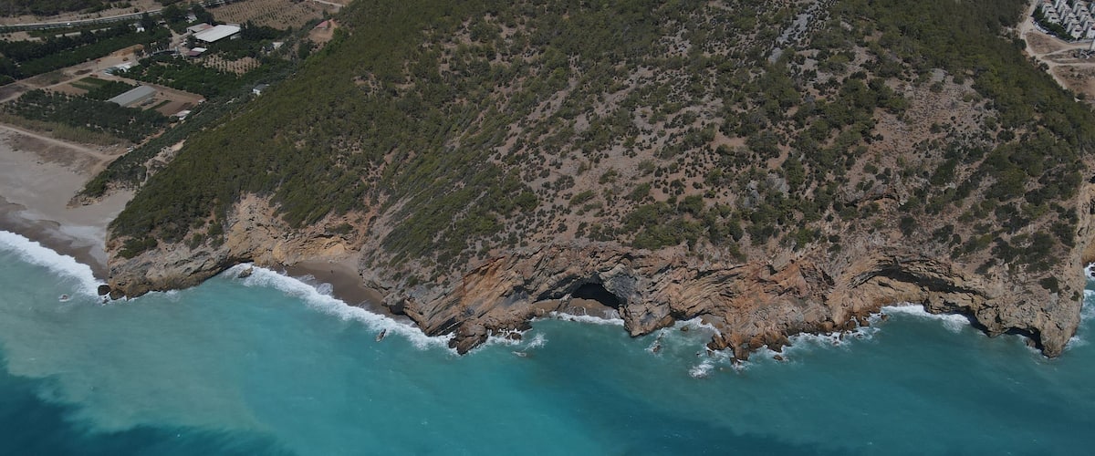 A coastal landscape with a rocky shoreline, clear turquoise waters, and a dense forested area.