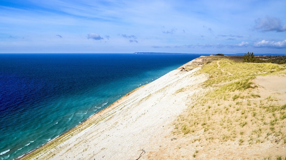 A coastal landscape with a sandy beach, grassy dunes, and a clear blue sea.