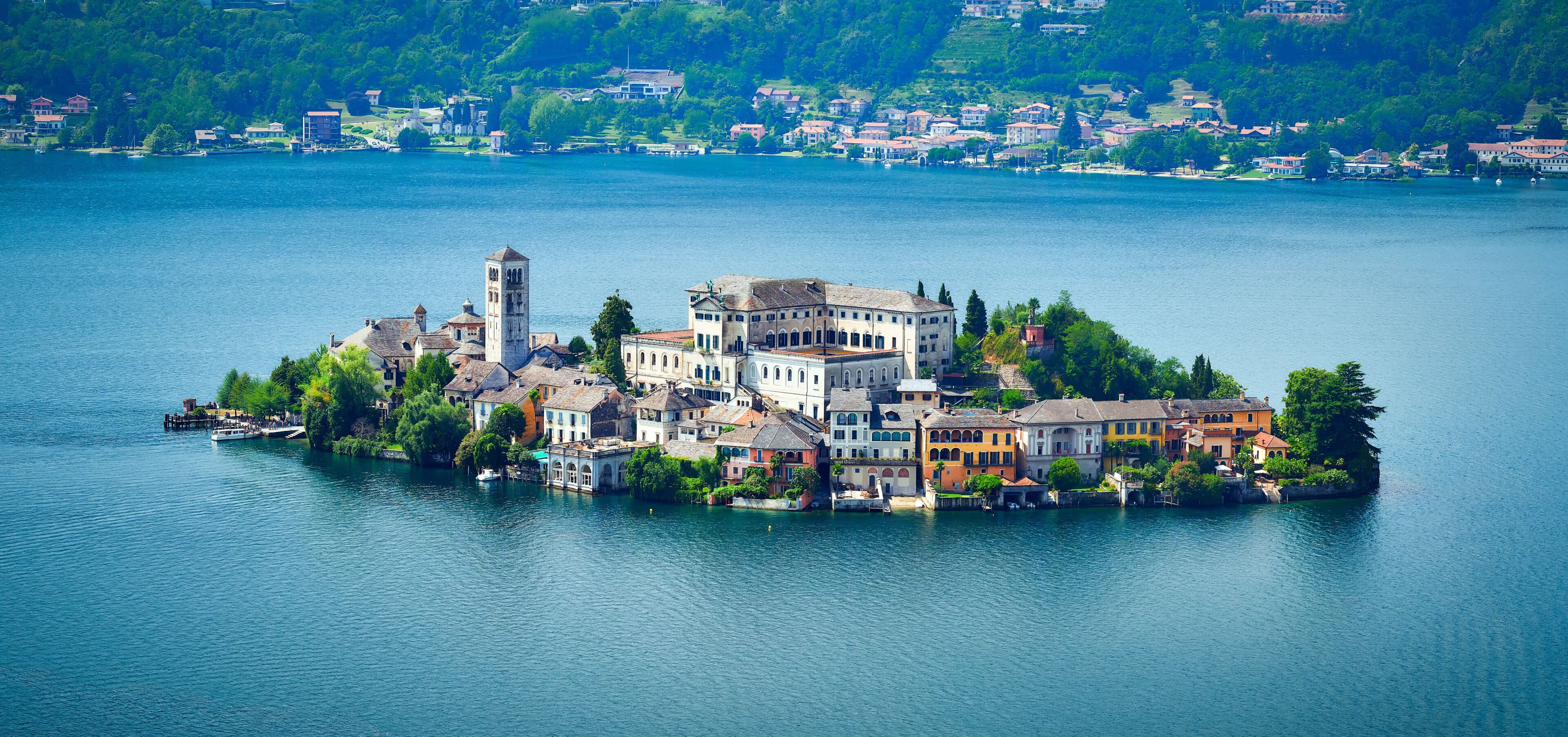 A lakeside town with historic buildings, a prominent tower, and lush greenery.