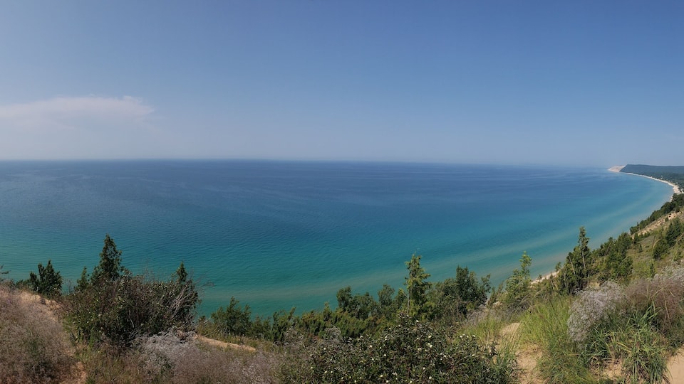 A coastal landscape with a sandy path, dense greenery, and a clear view of the ocean.