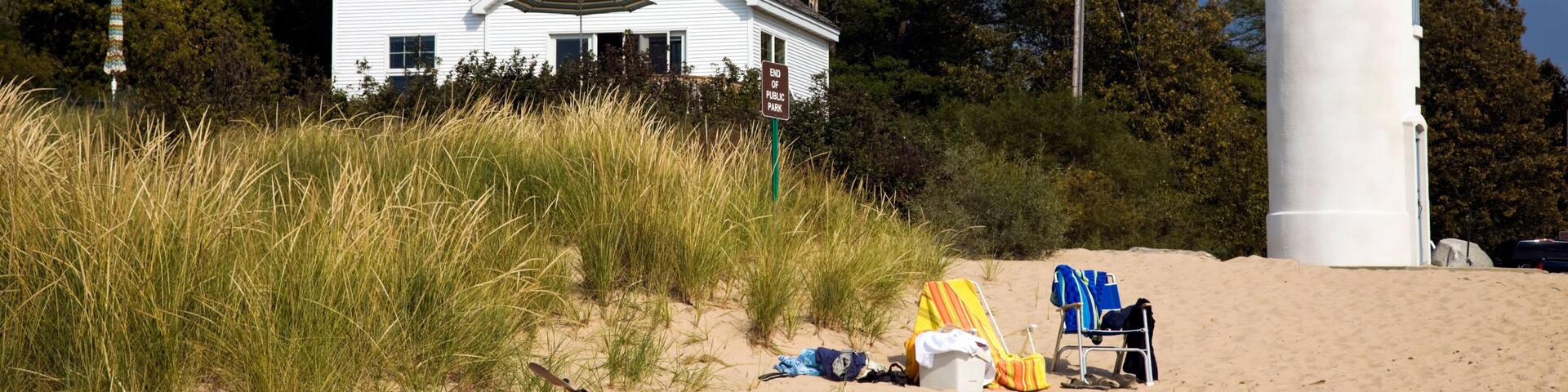 A white house, a lighthouse, and a red kayak on a sandy beach.