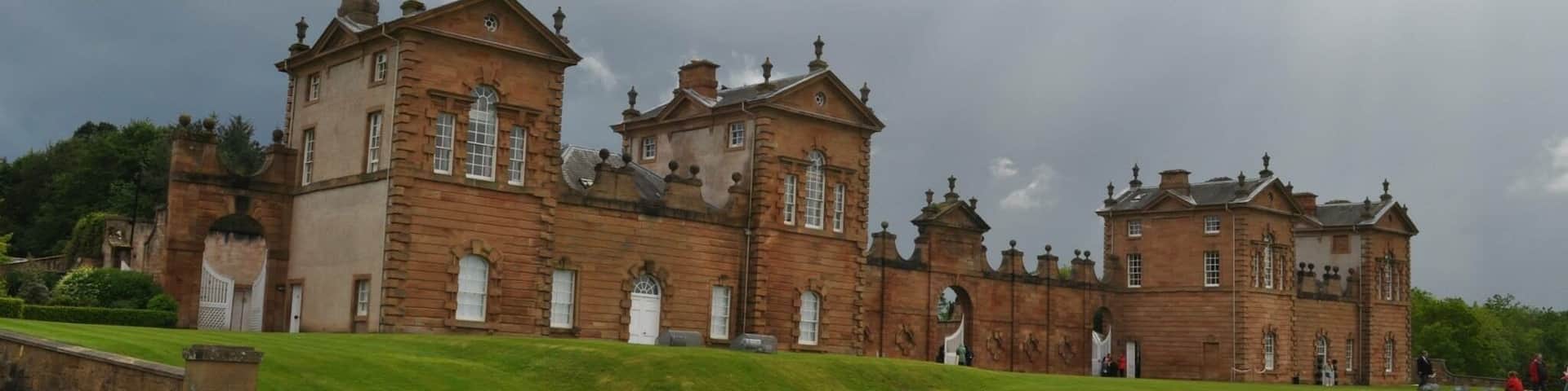 A large, historic stone building with multiple towers and arched windows, surrounded by a well-maintained lawn and a paved path.