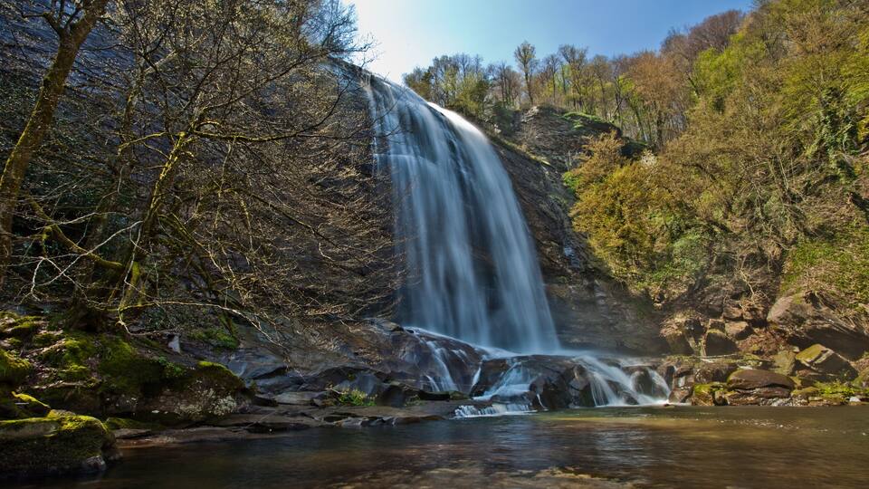 A waterfall cascading into a clear pool surrounded by rocky terrain and trees.