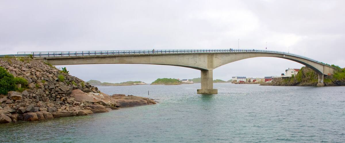A concrete bridge over a calm river with rocky shores and distant buildings.