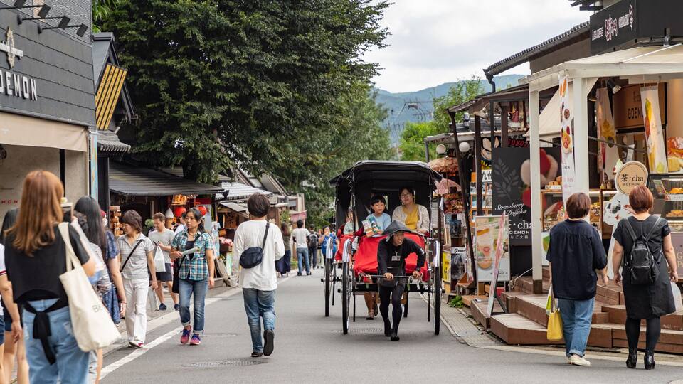 A bustling street with people walking, a traditional rickshaw, and various shops.