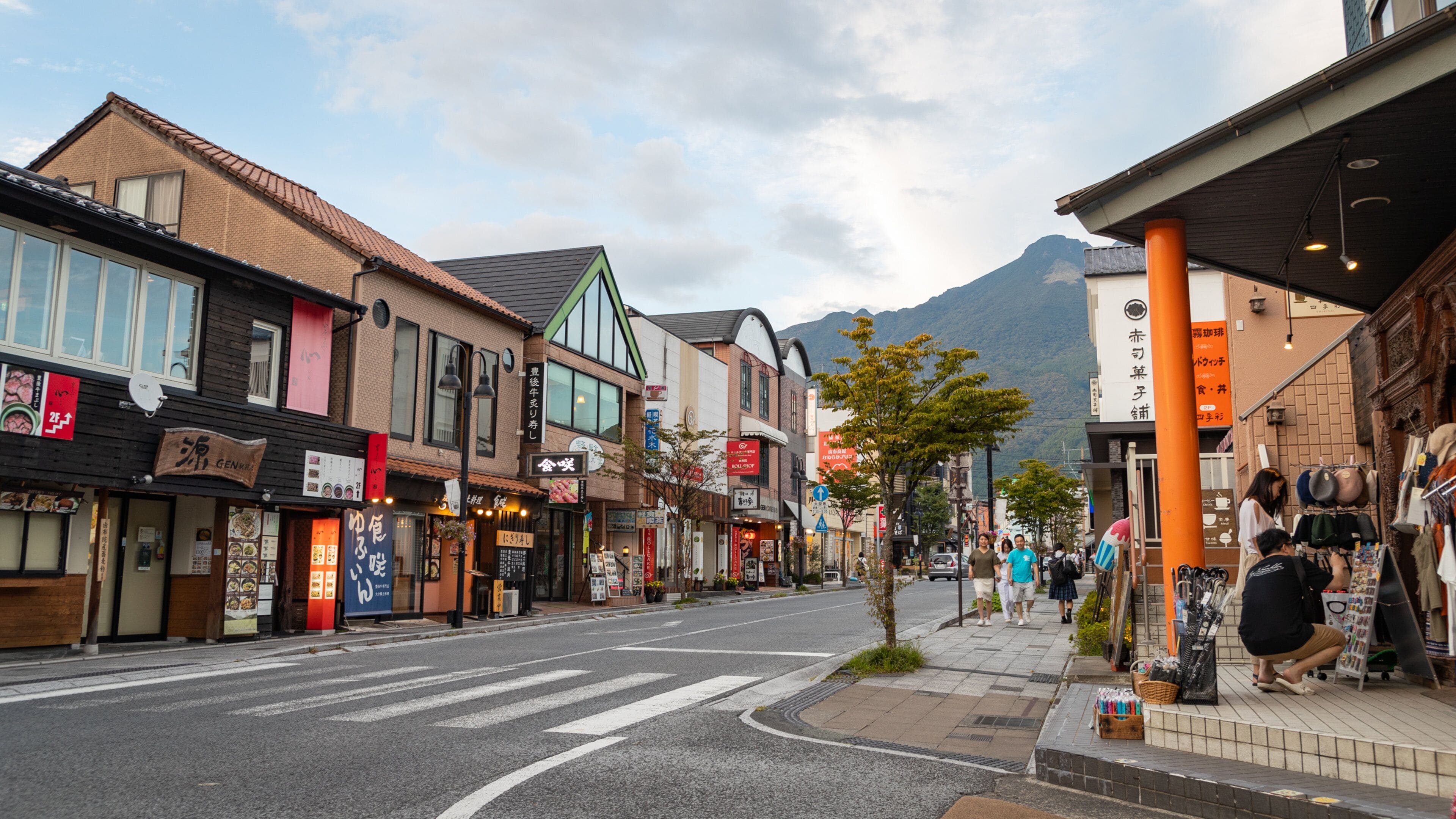A street lined with shops and restaurants, a crosswalk, and a mountain in the background.