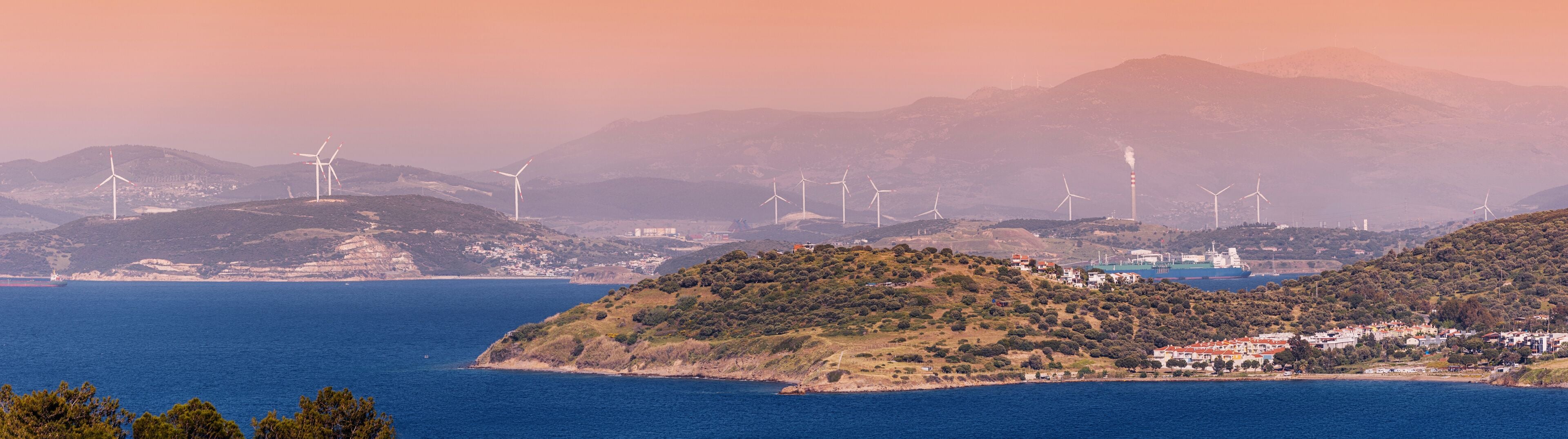 Wind farm generating renewable energy near the sea with a cargo ship sailing in the background