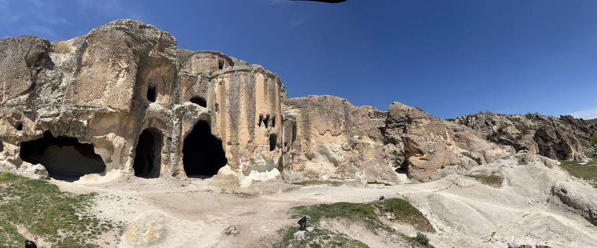 A large rock formation with multiple caves and a dirt path leading to it.
