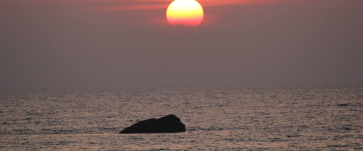 A sunset over the ocean with a rock in the foreground.