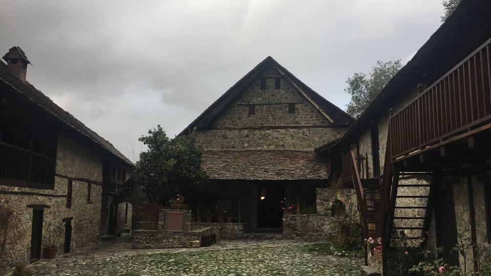 A stone building with a steep roof, surrounded by cobblestone paths and potted plants.