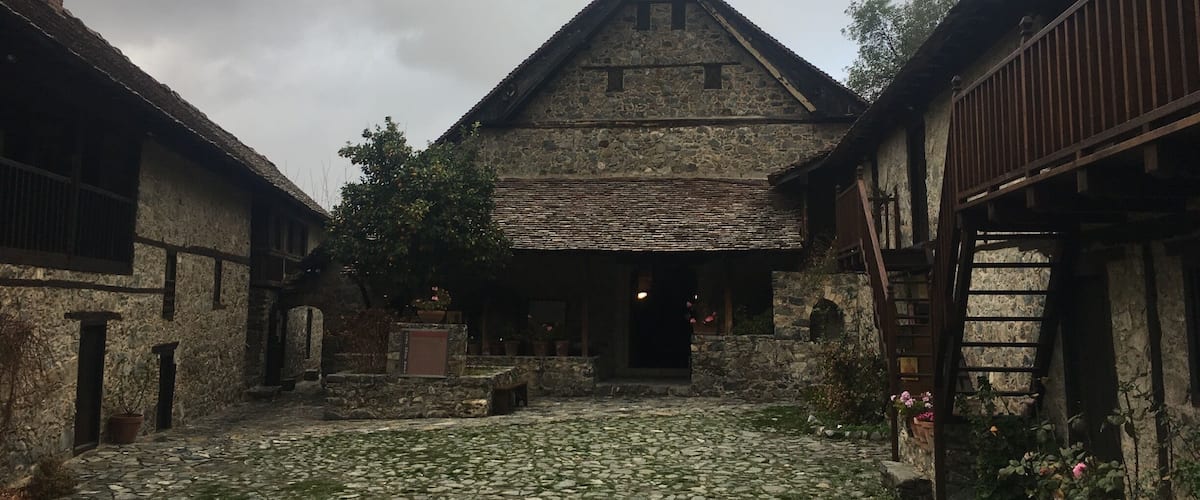 A stone building with a steep roof, surrounded by cobblestone paths and potted plants.