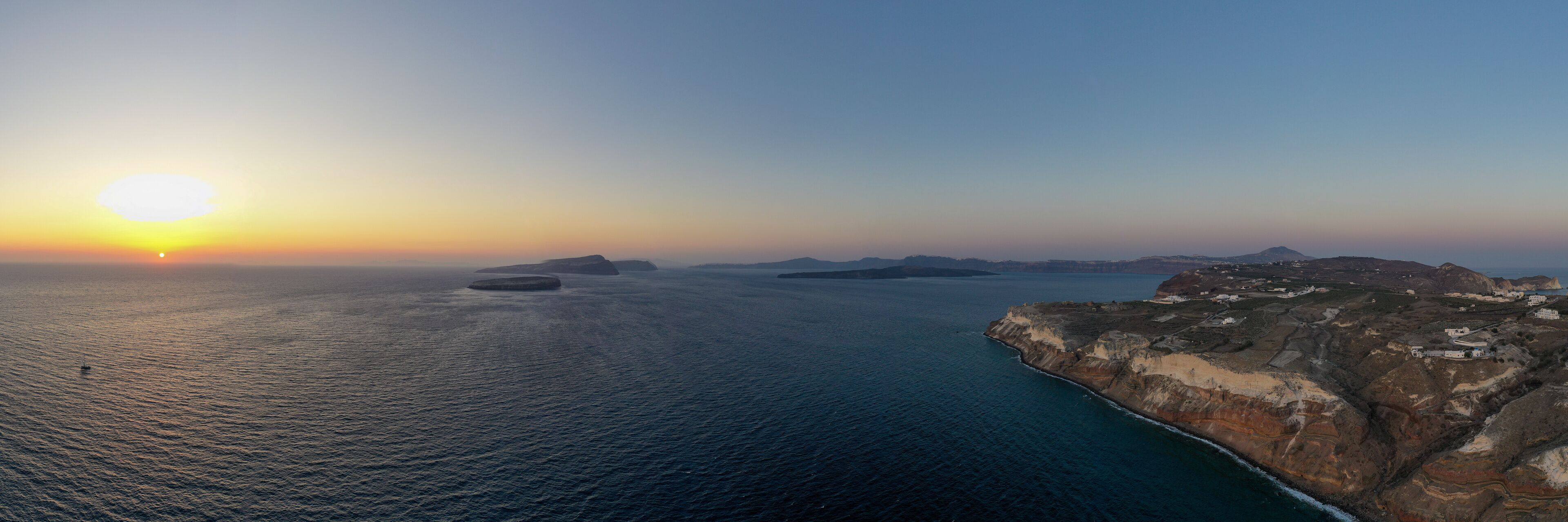 A coastal landscape with a sunset, rocky cliffs, and scattered islands.