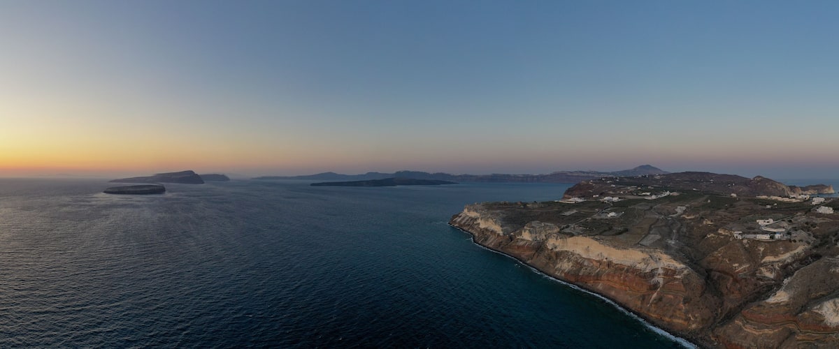 A coastal landscape with a sunset, rocky cliffs, and scattered islands.