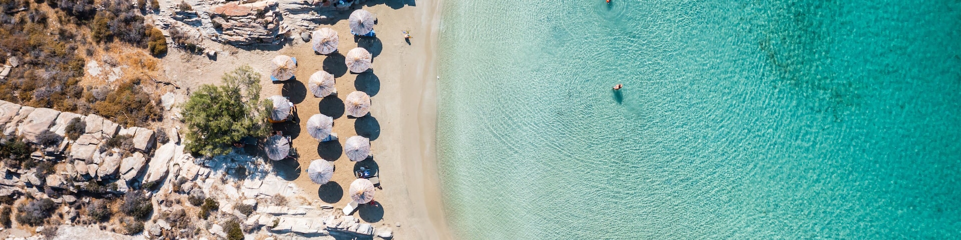 Una playa rocosa con agua turquesa cristalina, sombrillas y vegetación escasa.