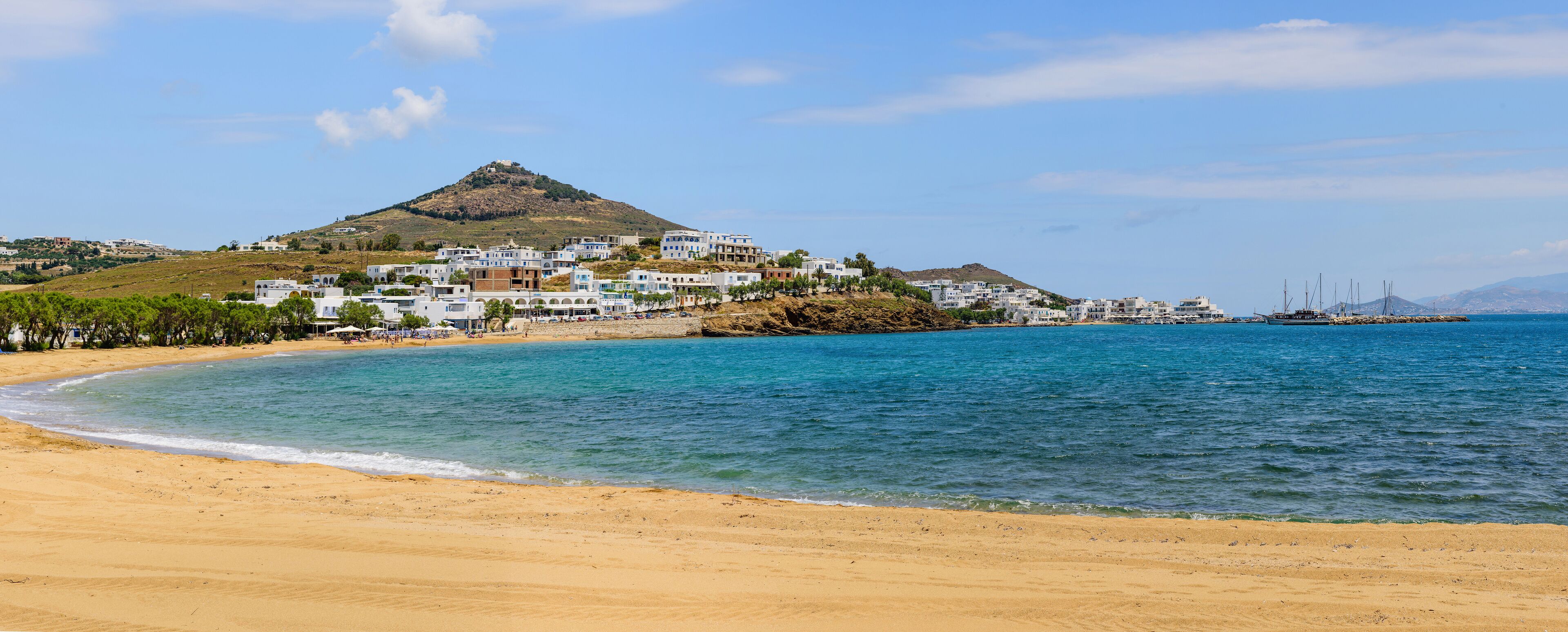 A coastal town with white buildings, a beach, and a hill in the background.