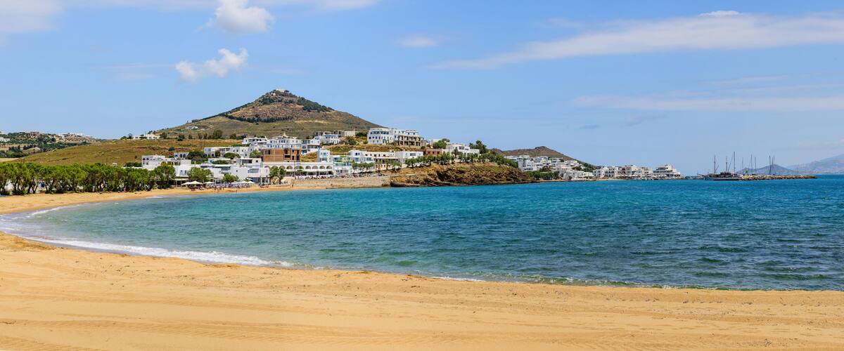 A coastal town with white buildings, a beach, and a hill in the background.