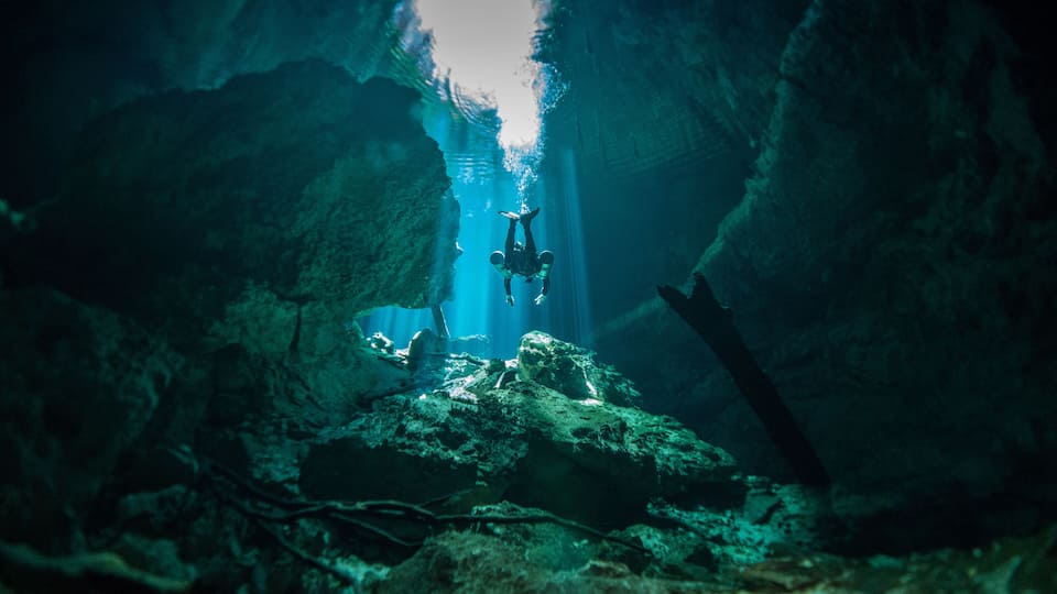 A diver in a cave with stalactites and stalagmites.