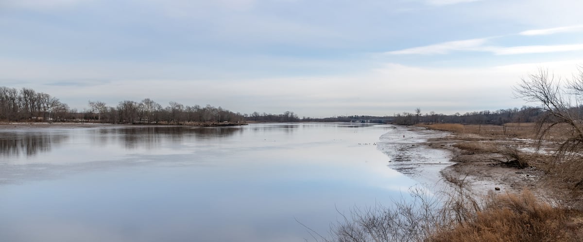 A calm river with a clear sky and sparse trees along the banks.