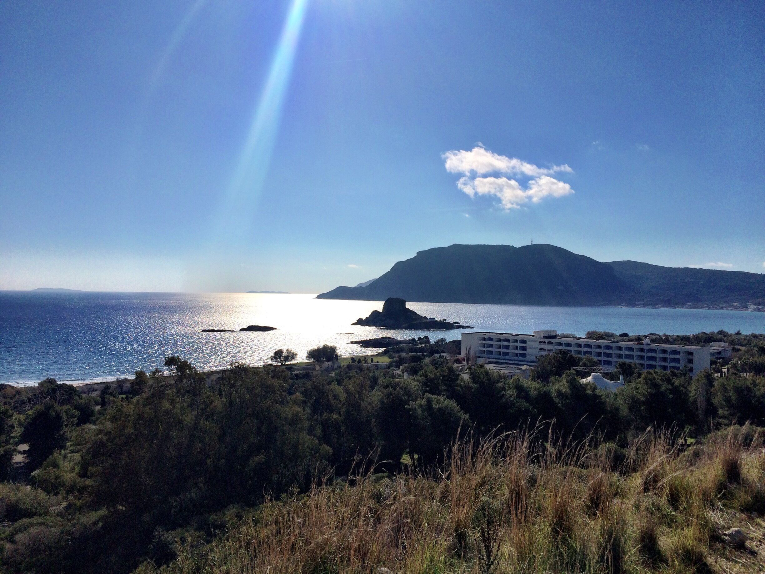 A coastal landscape with a clear sky, a mountain in the distance, and a building in the foreground.