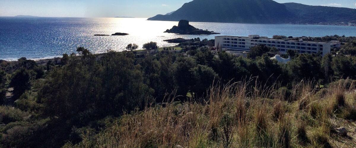A coastal landscape with a clear sky, a mountain in the distance, and a building in the foreground.