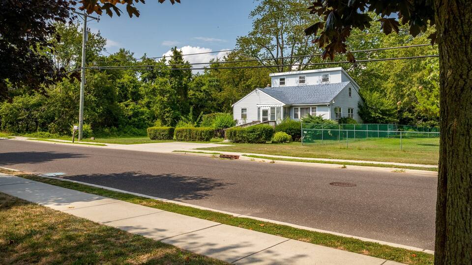 A two-story house with a gray roof, surrounded by lush green trees and a well-maintained lawn.