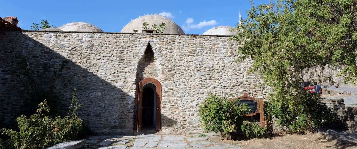 A stone wall with a wooden door and domed structures in the background.