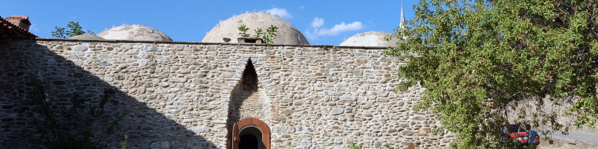A stone wall with a wooden door and domed structures in the background.