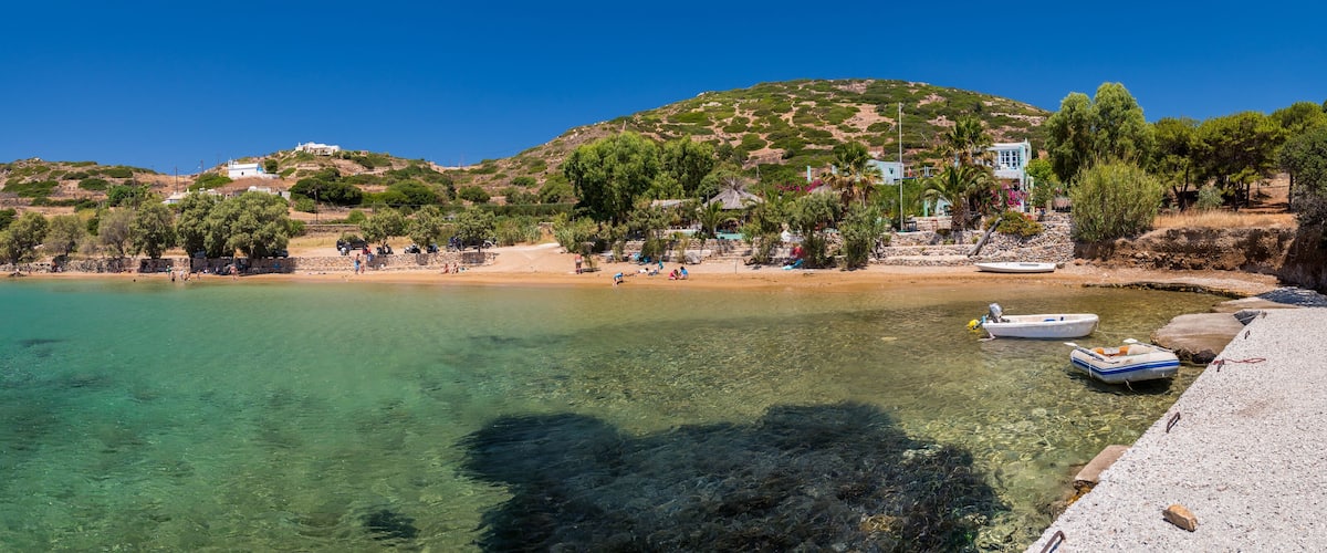 A clear coastal area with boats, a sandy beach, and buildings on a hillside.