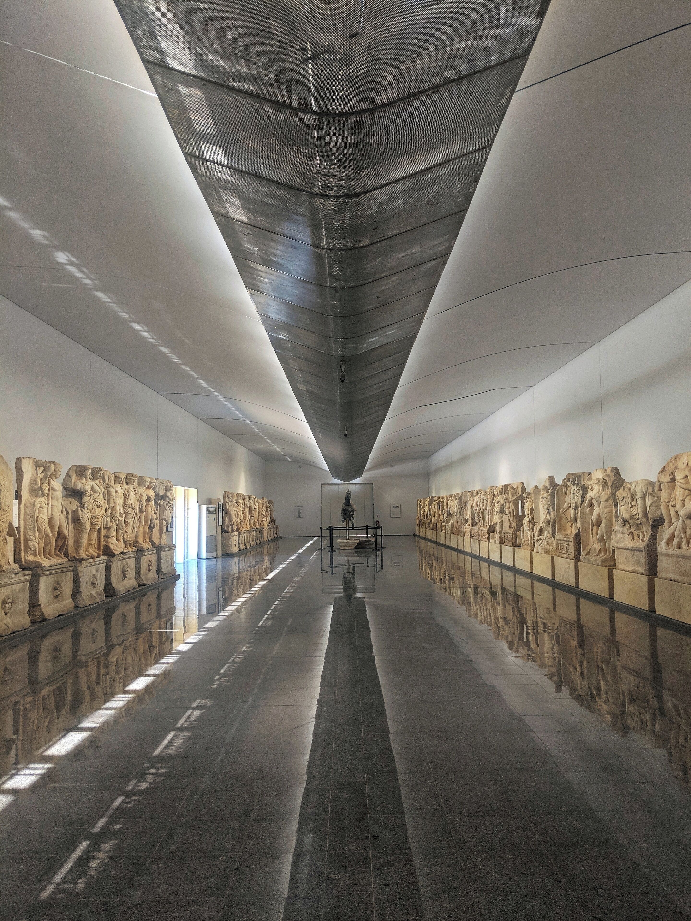 A long, dimly lit corridor with reflective floors and walls adorned with classical sculptures.