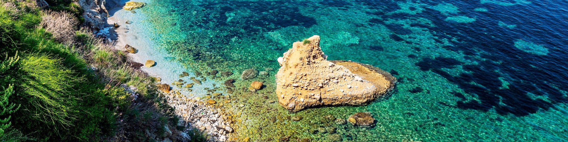 A coastal landscape with clear turquoise waters, rocky shorelines, and a white building on the left.