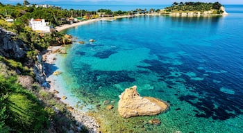 A coastal landscape with clear blue waters, rocky shorelines, and a white building on the left.