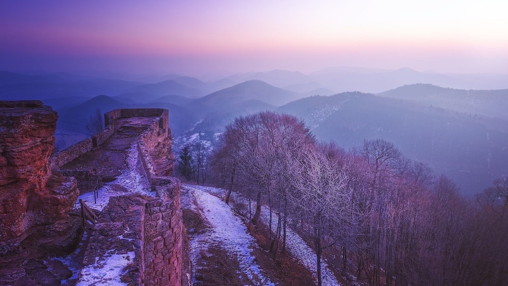 A stone wall and a snow-covered path in a mountainous area.
