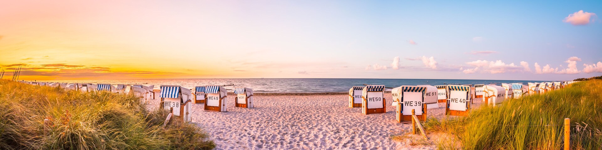 A beach with rows of beach chairs labeled with numbers, a sandy path leading to the sea, and a sunset in the background.