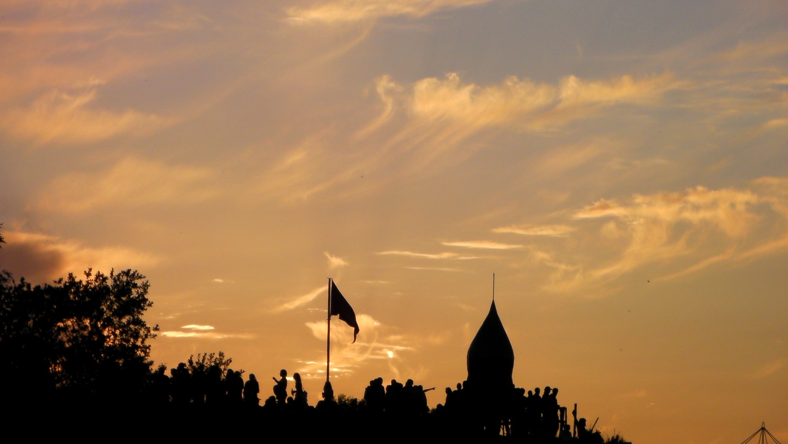 A silhouette of a crowd and a building with a flag against a sunset sky.