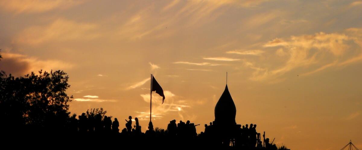 A silhouette of a crowd and a building with a flag against a sunset sky.