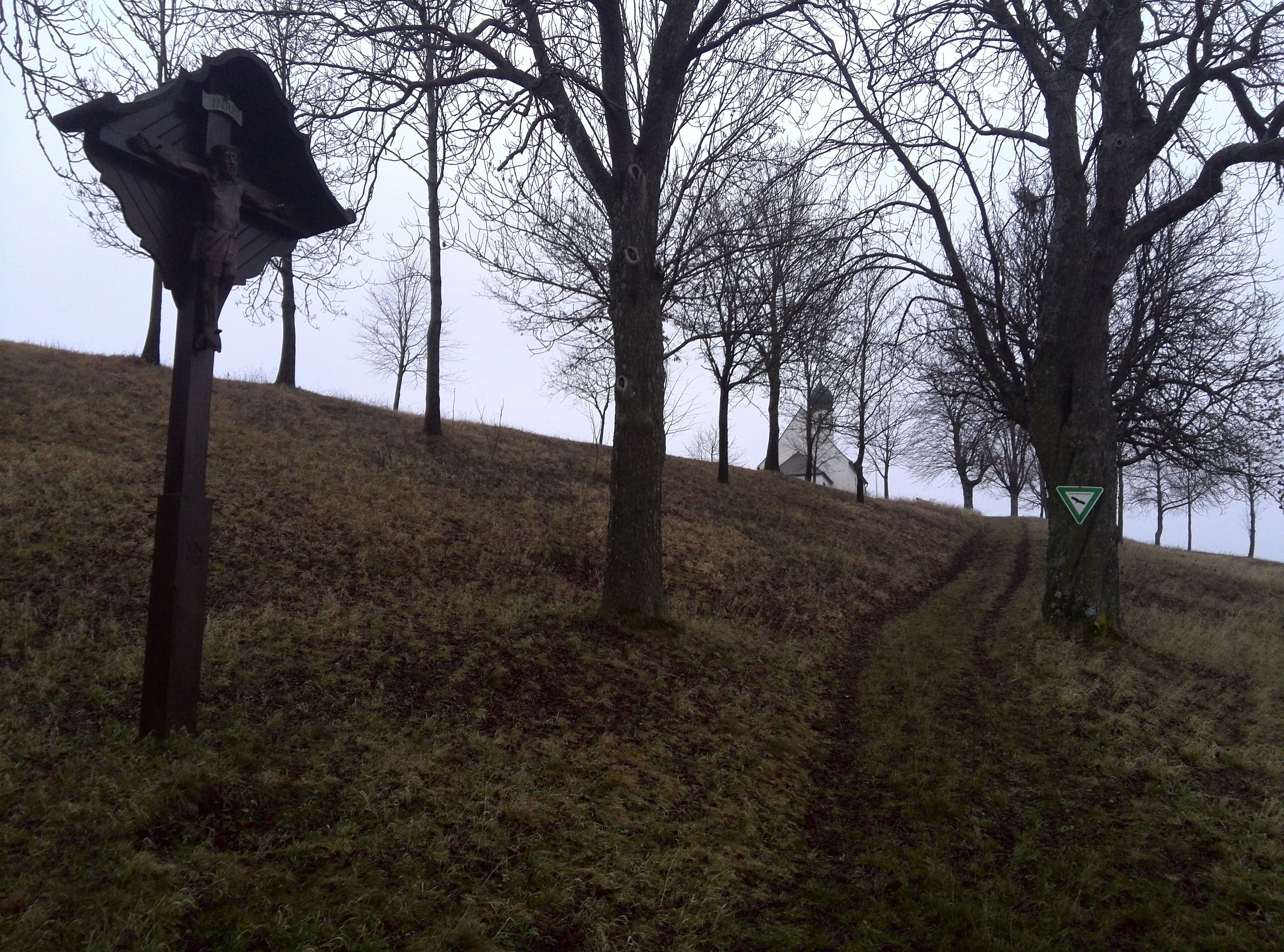 A hill with a windmill, a triangular warning sign, and leafless trees.