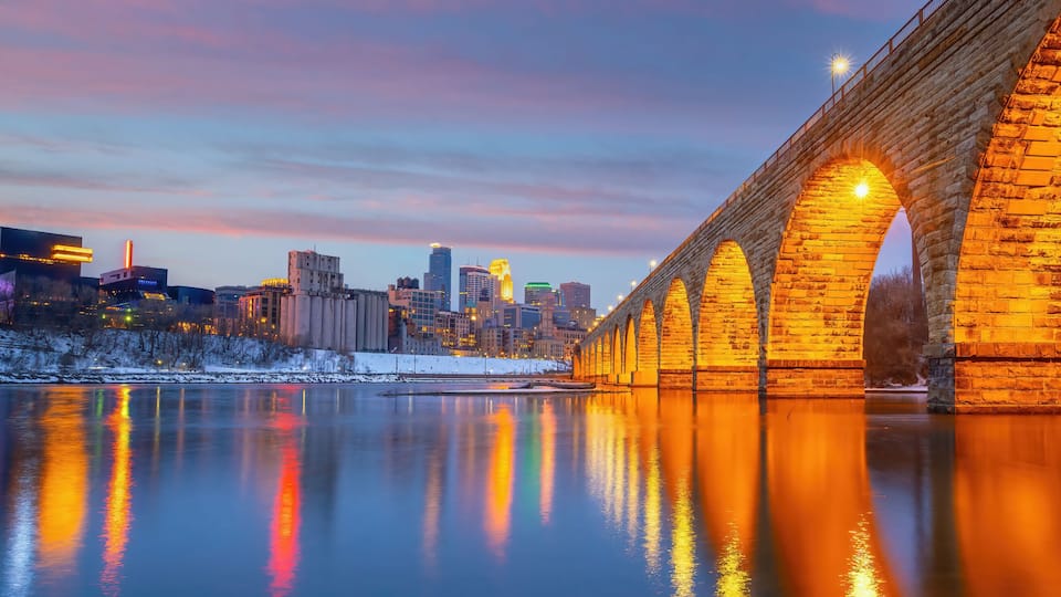 A stone bridge over a river reflecting city lights, with a city skyline in the background.
