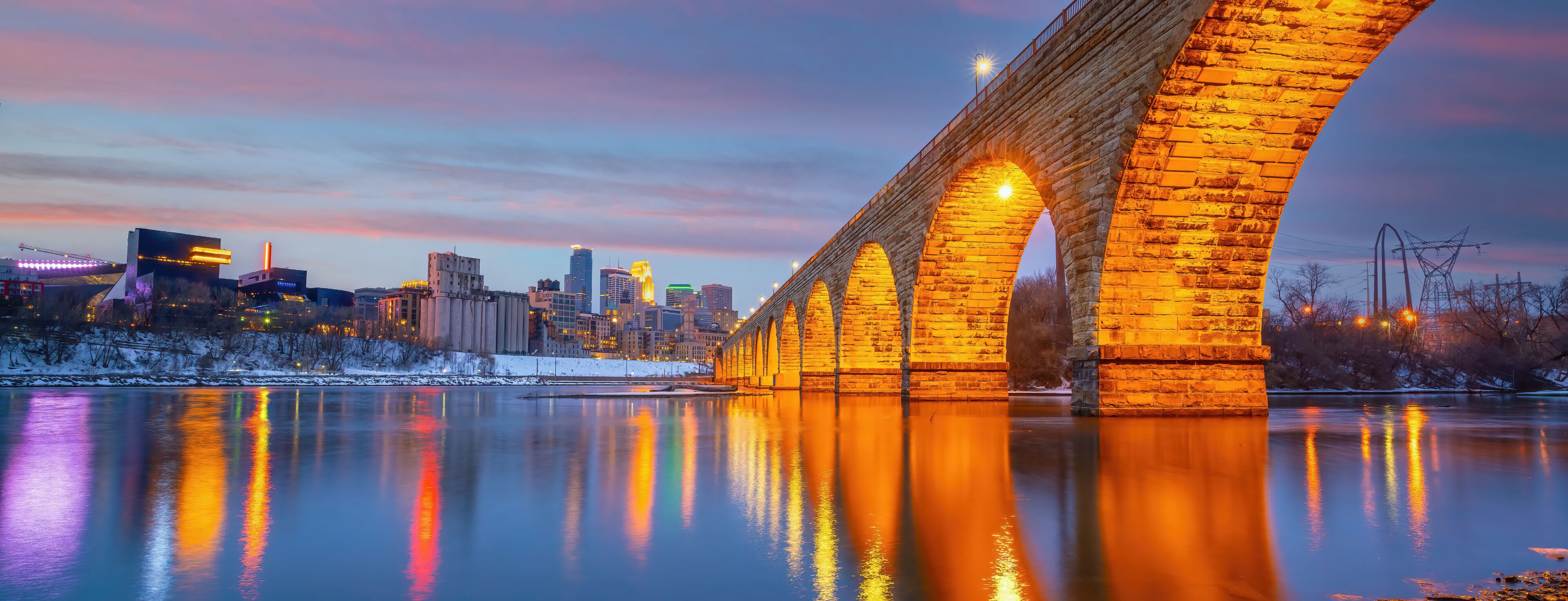 A stone bridge over a river reflecting city lights, with a city skyline in the background.