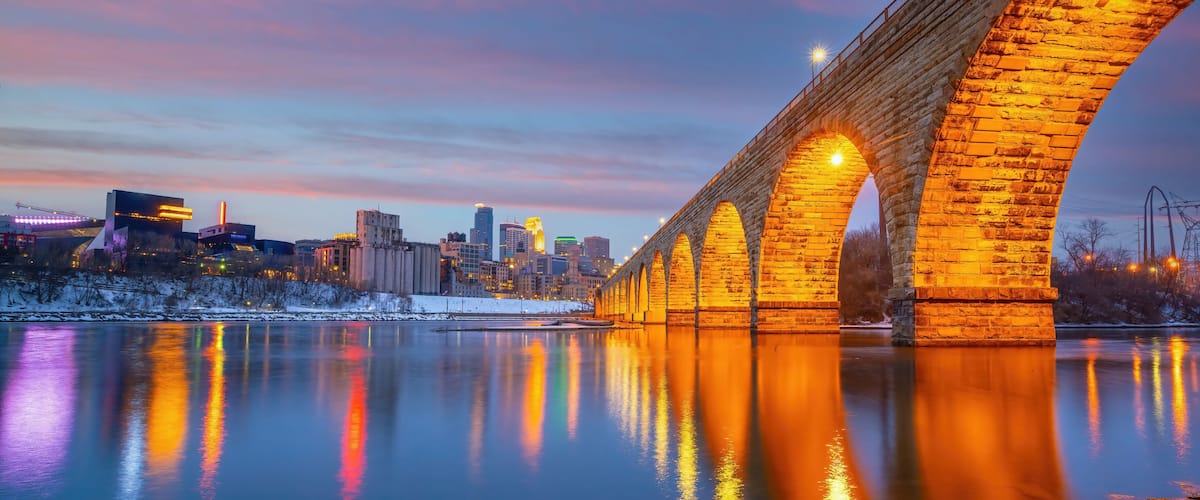 A stone bridge over a river reflecting city lights, with a city skyline in the background.