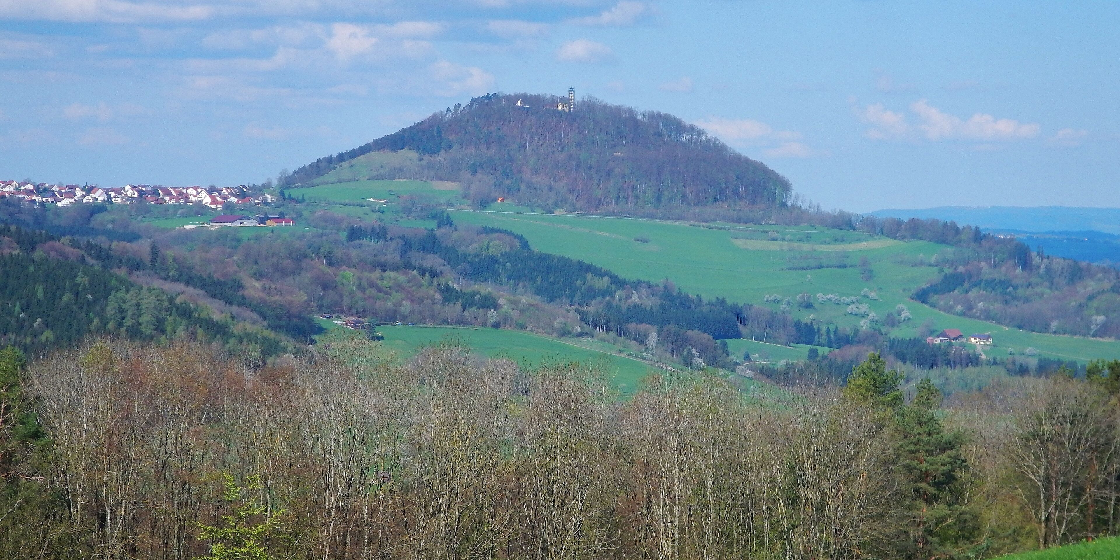 A hill with a small building on top, surrounded by green fields and trees.