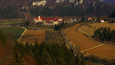 Paisaje rural con una gran propiedad que incluye un edificio de techo rojo, una iglesia y una vía de tren.