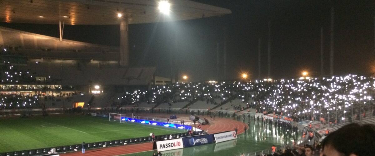 A stadium filled with spectators, a football pitch, and advertising banners.
